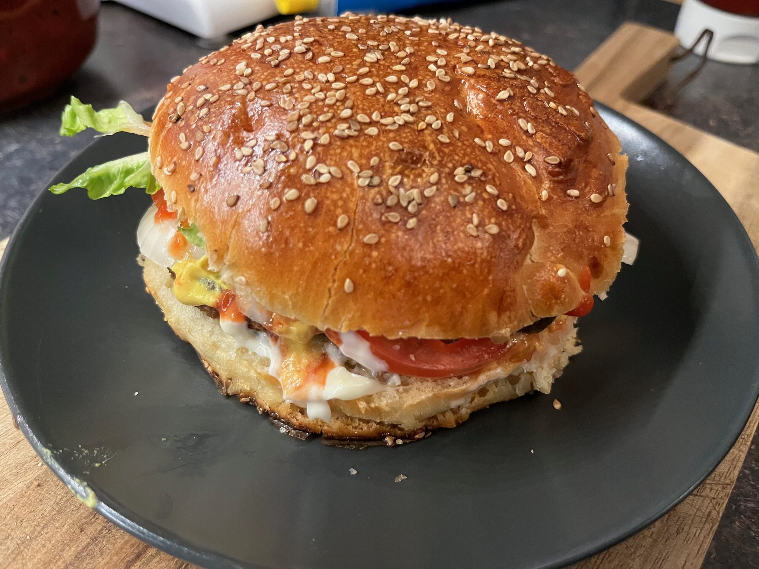 Fertiger veganer Burger auf schwarzem Teller mit selbst gebackenem Sesam-Bun, belegt mit Tomate, Salat und Soße