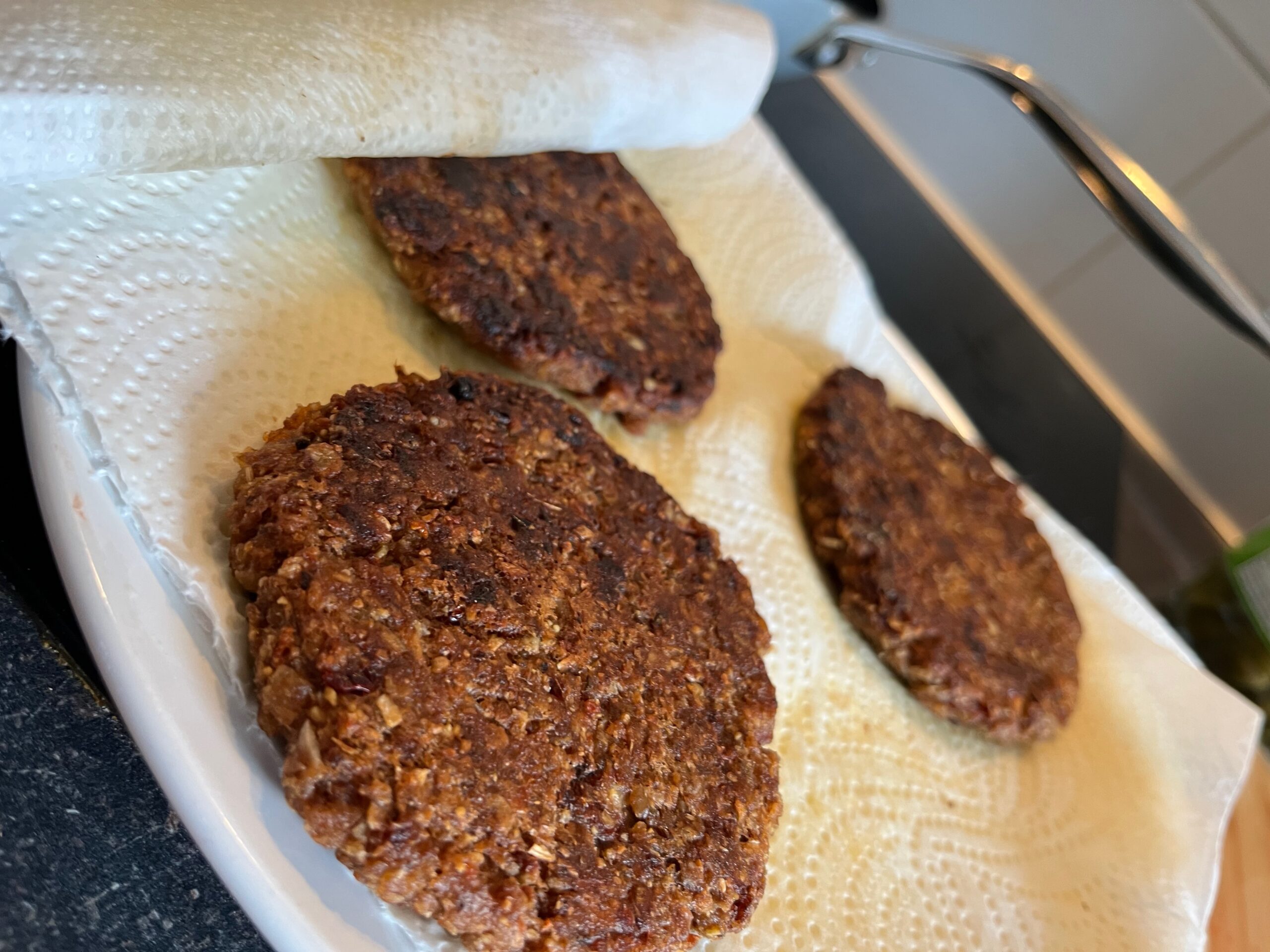 Drei gebratene vegane Hafer-Burger-Patties auf Küchenpapier abtropfend